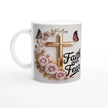 Close-up of faith-themed ceramic mug with pink roses, butterflies, and gold cross, on a wooden table with plants