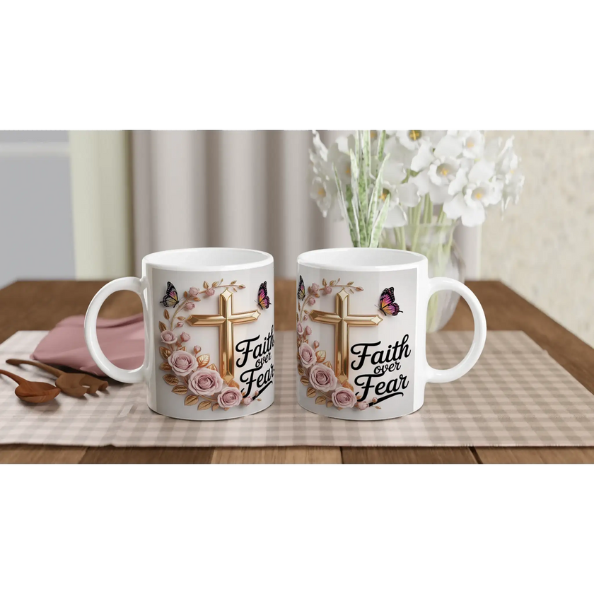 White ceramic mug with faith-themed design, pink roses, butterflies, and gold cross, on a wooden table with plants