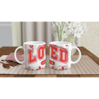 White ceramic mugs with red and pink geometric designs, on a checkered tablecloth with a pink napkin and wooden spoon