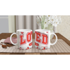 White ceramic mugs with red and pink geometric designs, on a checkered tablecloth with a pink napkin and wooden spoon